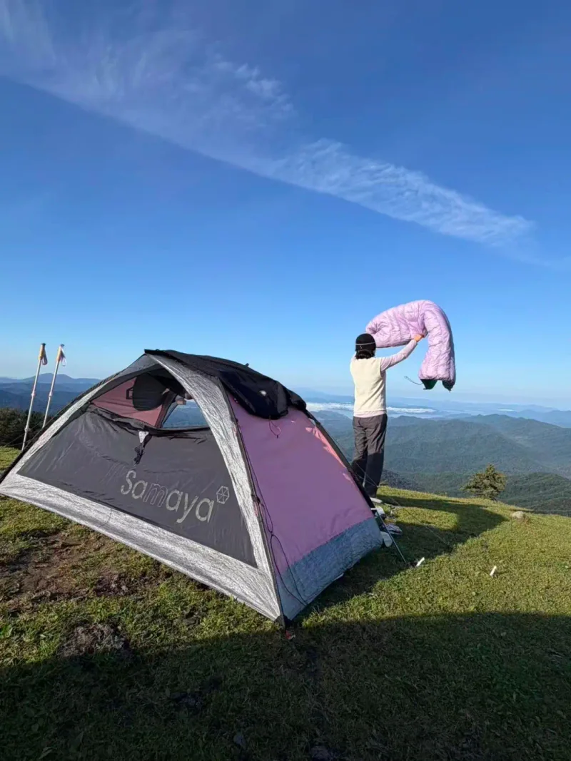山脊草地上的帐篷和正在整理装备的营友