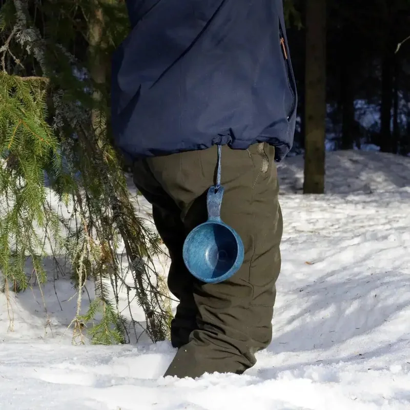 藍色短柄杯掛在雪林中行走者的褲側