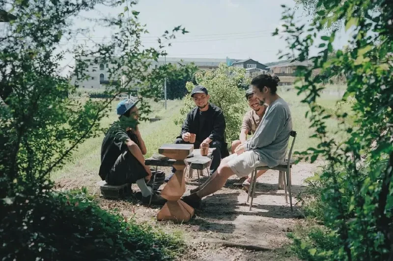Three people share drinks around an outdoor wooden table.