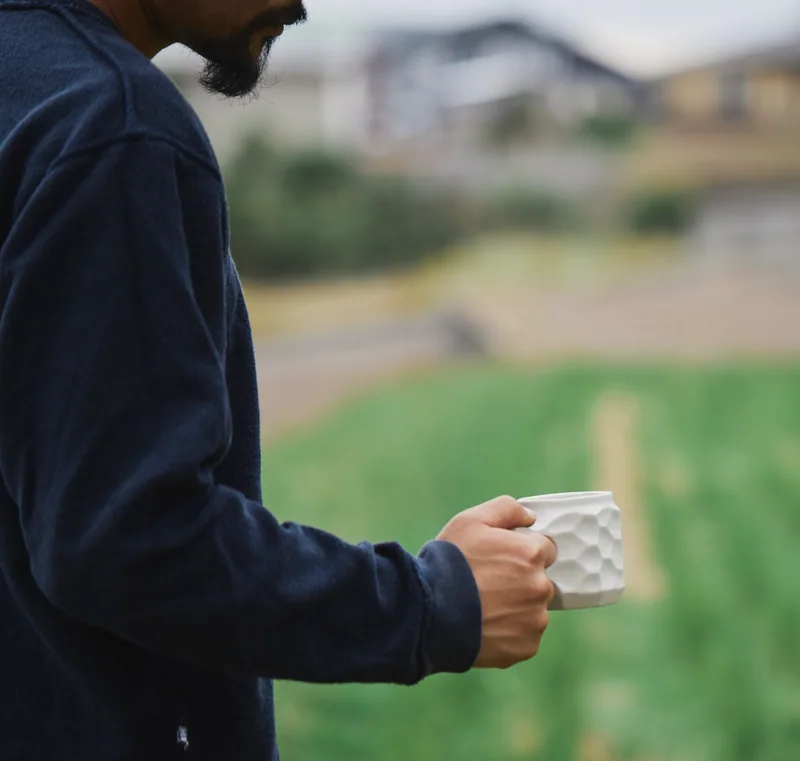 A person outdoors holds a textured white JINCUP.