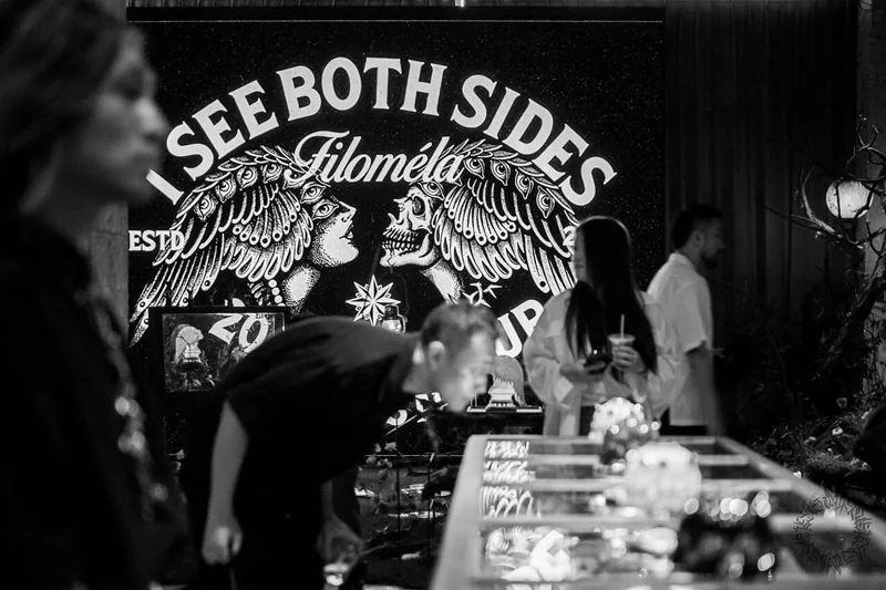 參觀者站在 I SEE BOTH SIDES 畫作和展櫃前的黑白照片