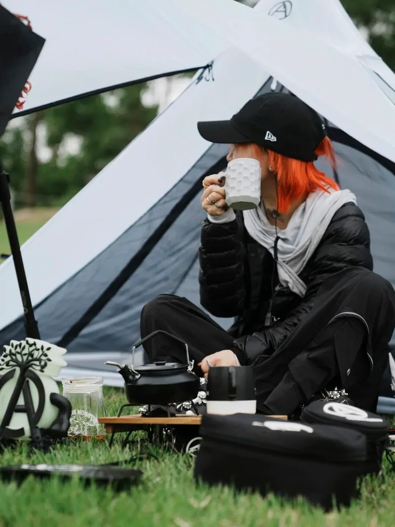 A camper uses a wooden cup beside a tent.