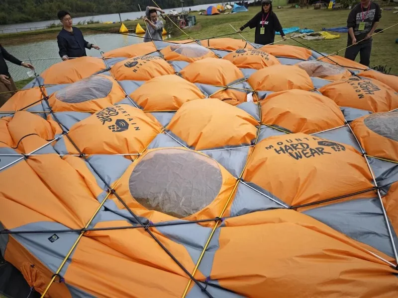 草地上平铺的橙色 Mountain Hardwear 大帐和交错杆件